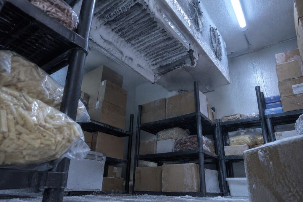 Vriescel van binnen met rijp op de verdamper en dozen diepvriesproduct op stellingen